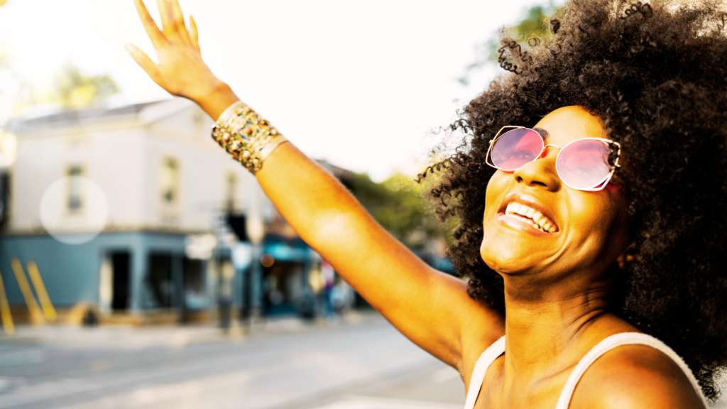 Beautiful Black woman with an Afro smiling and waving in the neighborhood.